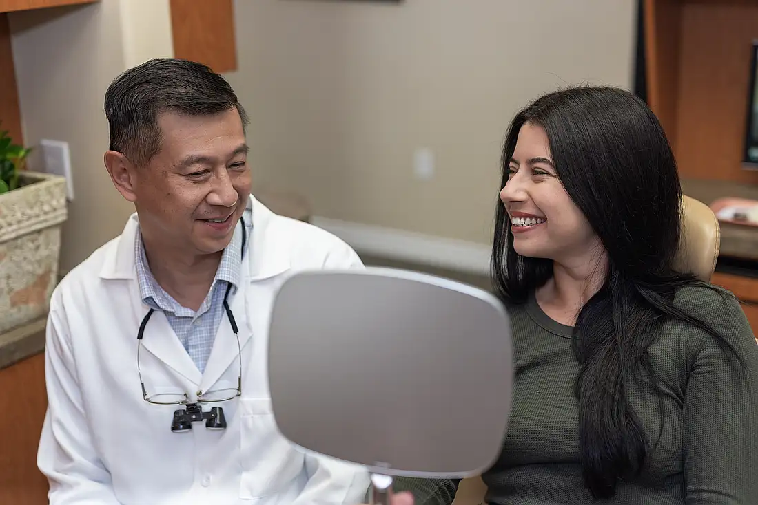 Dr. Tom Jou with a smiling patient holding a hand mirror