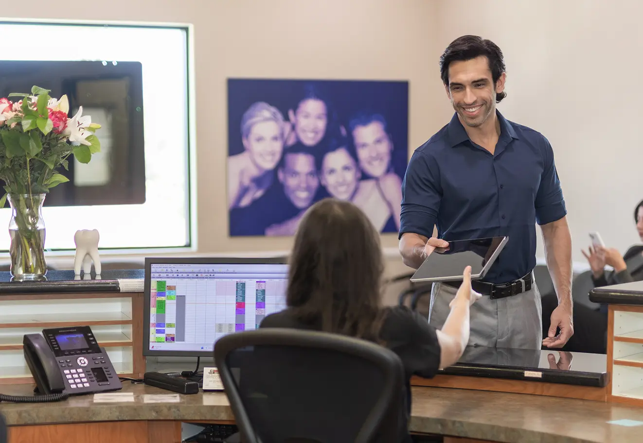 Smiling patient speaking with a receptionist at the dental office reception desk