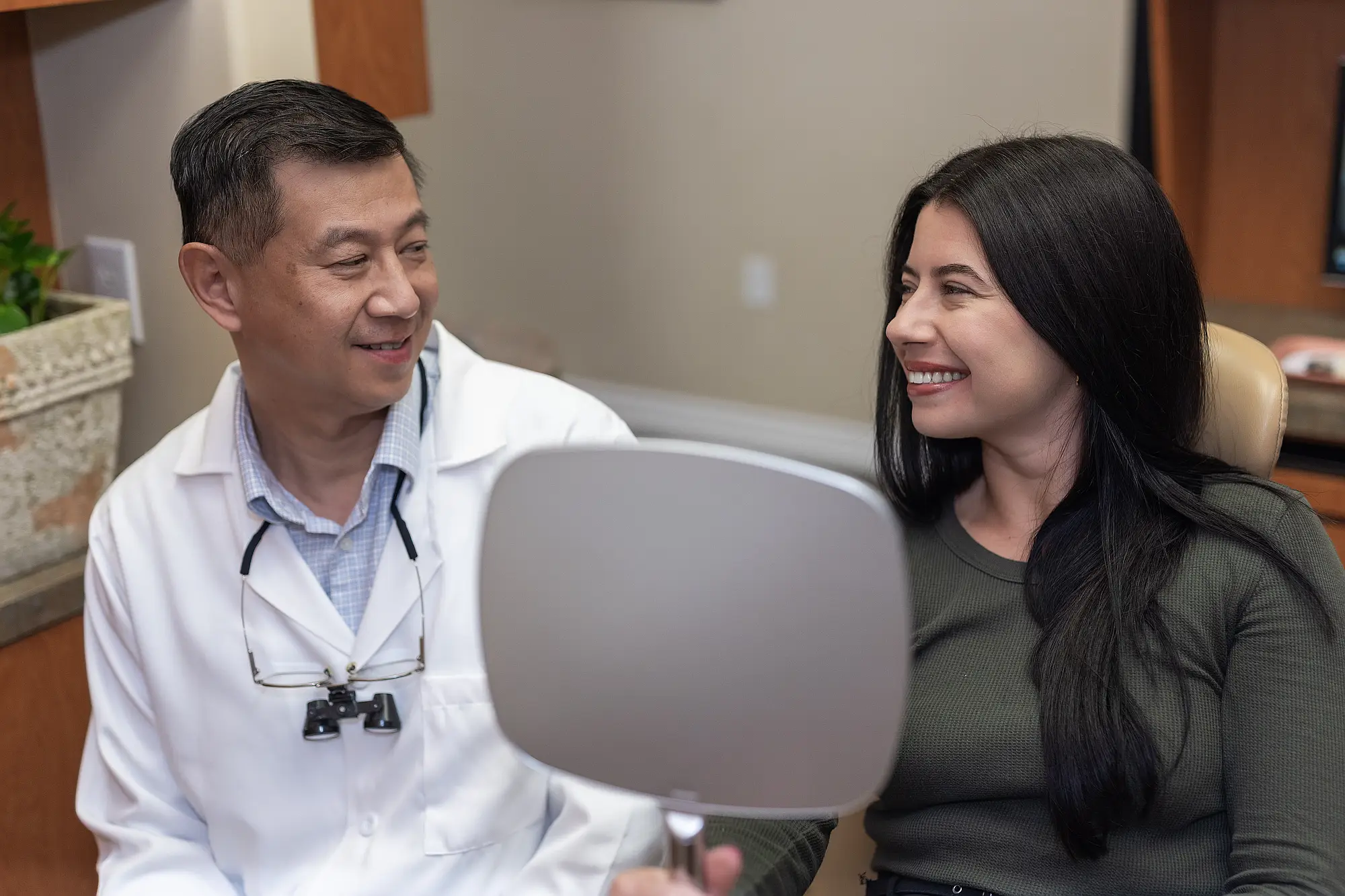 Dr. Tom Jou with a smiling patient holding a hand mirror